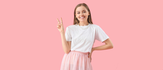 Happy young woman in t-shirt showing victory gesture on pink background