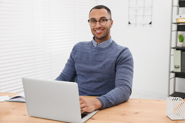 Happy young intern working with laptop at table in modern office