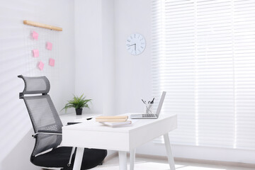 Desk and comfortable chair in modern office, space for text. Interior design