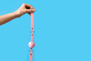 Woman with pink mouth gag from sex shop on blue background
