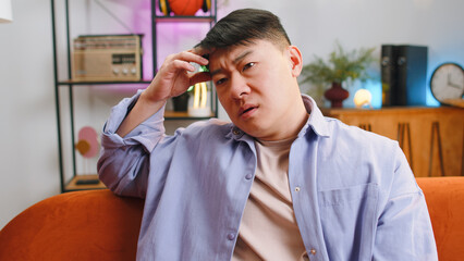 Sad lonely man sitting at home living room looks pensive thinks over life concerns, unrequited love...
