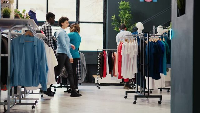 Fashionable couple shopping for elegant shirt, analyzing clothes material before buying it in modern boutique. Stylish customers looking at hangers with new fashion collection in clothing store - Powered by Adobe