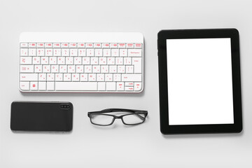 Composition with tablet computer, glasses, keyboard and mobile phone on white background