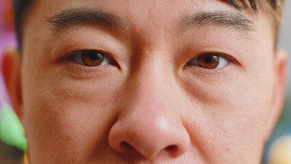 Extreme close-up macro portrait of smiling asian man face. Middle-aged guy eyes looking at camera. Adult positive chinese man opening wide his closed eyes. Brown eyes of brunette male attractive model