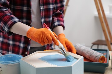 Woman painting honeycomb shaped shelf with brush at table indoors, closeup