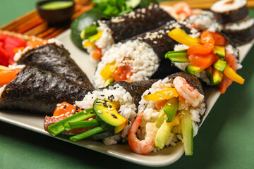 Plate with tasty sushi cones and rolls on green background, closeup