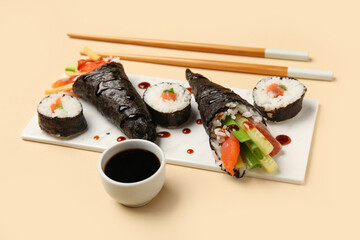 Board with tasty sushi cones, rolls, soy sauce and chopsticks on color background