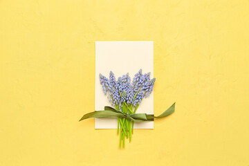 Blank greeting card with beautiful Muscari flowers and satin ribbon on yellow background