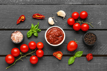 Composition with bowl of delicious tomato sauce and ingredients on black wooden table