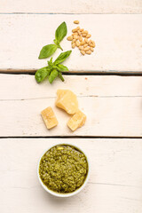 Composition with bowl of pesto sauce and ingredients on white wooden table