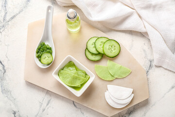 Board with cotton under-eye patches, dropper bottle and cucumber slices on grunge background
