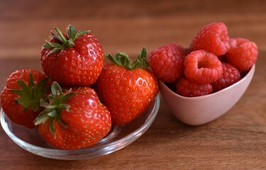 harvest of raspberries and strawberries in small cups on a wooden table