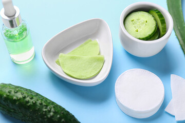 Bowls with cotton under-eye patches, cucumber and dropper bottle on blue background