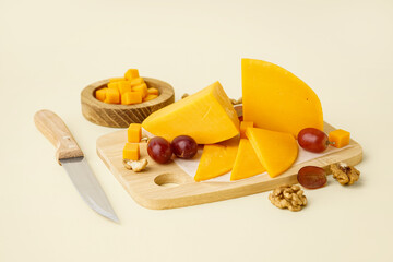 Board with tasty cheddar cheese, grapes and nuts on beige background