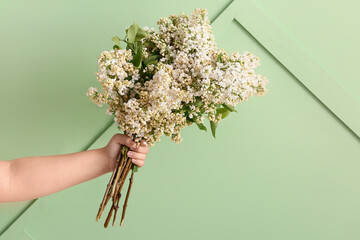 Female hand with bouquet of lilac flowers on green background