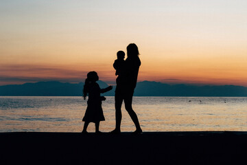 Mother with her girls enjoying the sunset on a beautiful beach on Mother's Day - obrazy, fototapety, plakaty