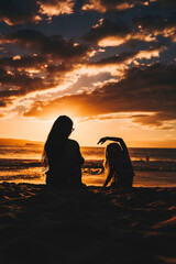 Mother with her daughter enjoying the beautiful orange sunset on the beach on Mother's Day - obrazy, fototapety, plakaty