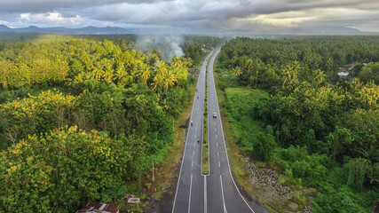 Aerial photo of the highway dividing the forest and villages with a mountain background.