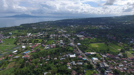 Aerial photo of the atmosphere of a village settlement among coconut trees, with the sea and mountains in the distance in the background.