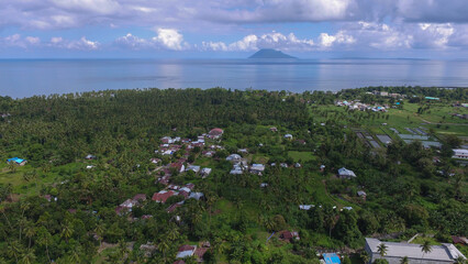 Fototapeta na wymiar Aerial photo of the atmosphere of a village settlement among coconut trees, with the sea and mountains in the distance in the background.