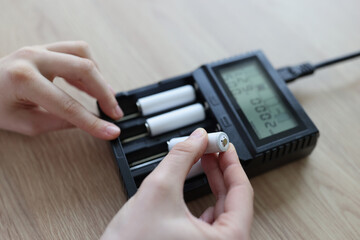 Female hands insert cells into charger on wooden table