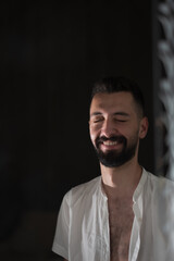 Fototapeta premium A young man with an open shirt laughs cheerfully. A single light illuminates his face.