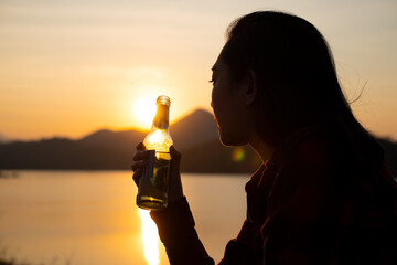 Silhouette woman holding a beer bottle on the beach at sunset