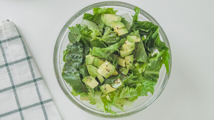 Romaine lettuce, celery, and avocado salad in a glass bowl on white kitchen table, view from above