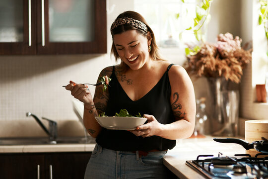 Woman, diet and person eating salad in her home kitchen and is happy for a meal with nutrition or healthy lunch. Smile, food and young female vegan in her apartment or house and eat vegetables - Powered by Adobe