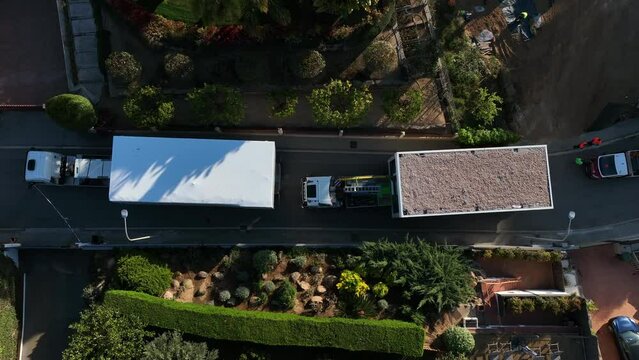 Trucks carrying prefabricated home modules in residential and luxury neighborhood. Aerial top-down sideways directly above