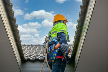 A Construction workers fixing house roof tiles wearing safety clothes and holding electric drill going up to install and repair roof tiles. House and building design projects