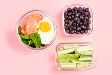 Food in glass lunch boxes on pink background close-up, top view.