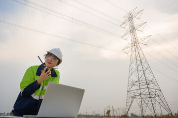 A female electrical engineer using a laptop computer standing at the electricity station to see the electric power production plan at high voltage electrode.