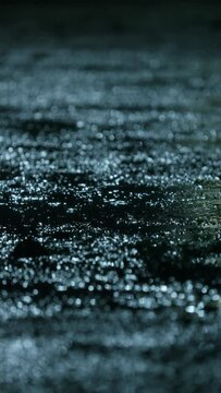 Closeup of rain drops falling on puddle with lights reflection on city sidewalk, Rain drop with street lights at night, Weather or environment, Nobody, Vertical video for smartphone footage