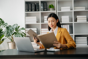 Confident Asian woman with a smile standing holding notepad and tablet at the office..