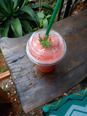 Strawberry smoothie in a plastic cup on a wooden table and green leaf in the garden of a roadside cafe. Top view. 
