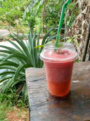 Strawberry smoothie in a plastic cup on a wooden table in the garden of a roadside cafe.