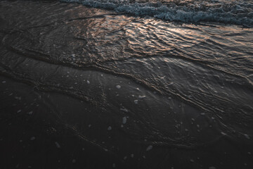 Calm waves on the dark wet sand at a beach at sunrise