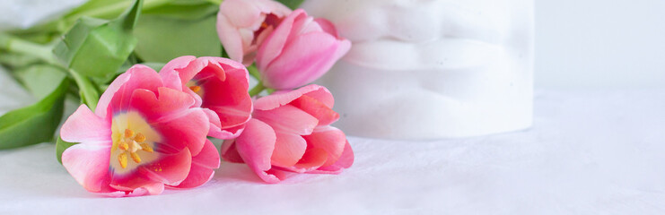 Pink tulips bouquet and plaster statue of lips lying on white wrinkled blanket background copy space