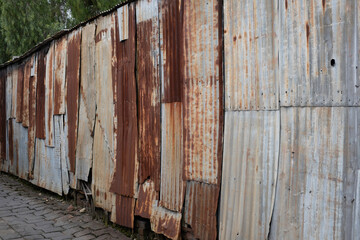Wall or fence in an alley made of rusted iron sheet metal and corrugated iron that are fastened...