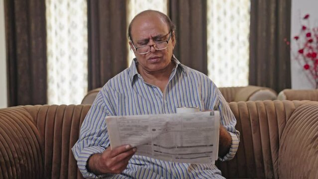 Upset Indian old man reading newspaper in morning