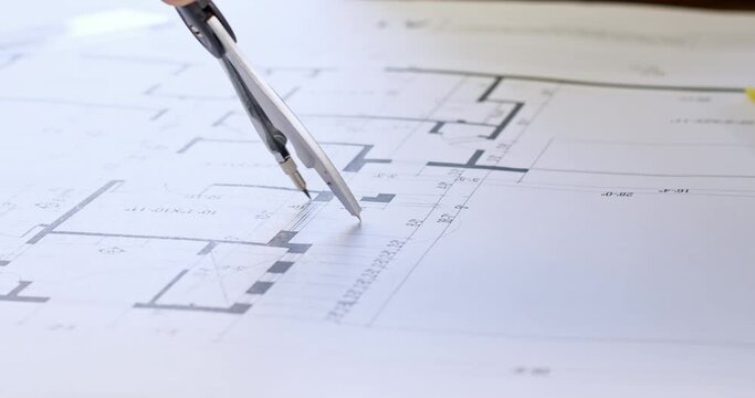 Skilled person attentively draws circle on paper building project using dividers with lead kernel. Yellow notebook and calculator lie on draft