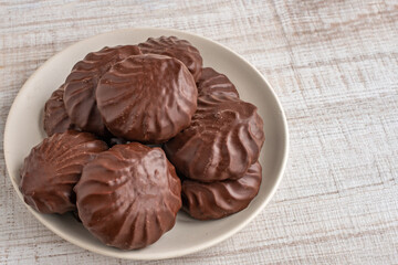 A close-up heap of chocolate marshmallows lying on a white glass plate. The concept of the negative impact of sweets and sweets on dental health