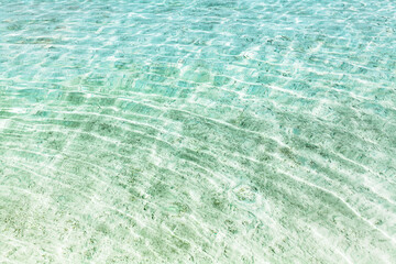 Sea water waves texture, ripples on water surface, transparent light blue ocean water, crystal clear aqua background top view, sun shine reflection, white sand bottom underwater, tropical island beach