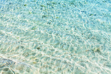 Sea water waves texture, ripples on water surface, transparent light blue ocean water top view, clear aqua background, sun glow reflection, white sand bottom, stones underwater, tropical island beach