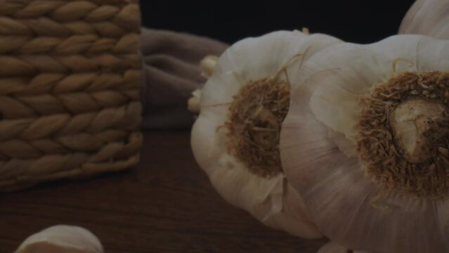 Dolly out macro close up of several garlic heads resting on a wooden table with dim lighting