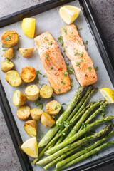 Homemade salmon fillet baked with asparagus and new potatoes with herbs and lemon close-up in a...