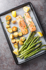 Baked spicy salmon fillet with asparagus and potatoes close-up in a baking sheet on the table. Vertical top vew from above