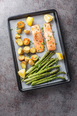 Healthy food baked salmon fillet with asparagus and potatoes close-up in a baking sheet on the table. Vertical top vew from above