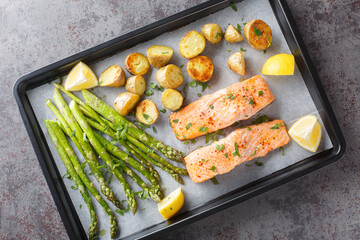 Delicious healthy salmon fillet baked with asparagus and new potatoes close-up in a baking sheet on the table. horizontal top vew from above